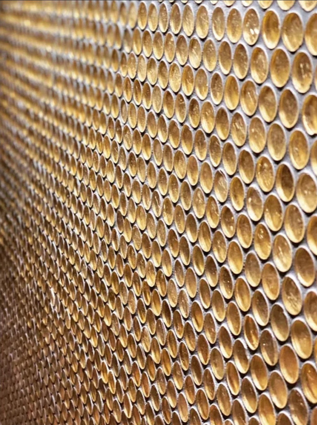 Gold glossy penny round glass mosaic tile sheet with mesh backing, angle view of installed wall